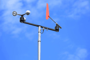 Anemometer measuring wind speed against a clear sky.