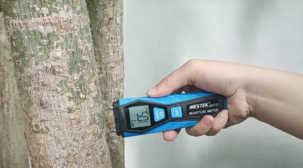 The image depicts a needle moisture meter testing the moisture content of wood.